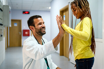 Wall Mural - Happy little girl and paediatrician doing high five after medical checkup in hospital