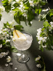 Wall Mural - Beautiful drink with ice liquor or gin,tonic and pear surrounded by flowering branches on green background.Close up of spring cocktail.