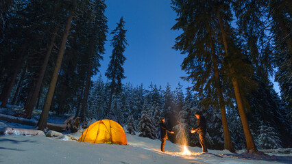 Wall Mural - couple camping with campfire and tent outdoors in winter forest