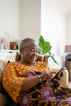 Smiling senior woman sitting on sofa with smart phone