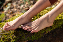 Bare Feet Of Woman Sitting On Moss Covered Log