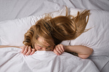 Wall Mural - Woman sleeps in bed. A girl with blond hair under a blanket on a pillow. Get up. Dream. Happy morning in the bedroom. Cozy and comfortable. Pillow blanket. Recovery, rest, lifestyle