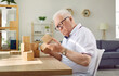 © Studio Romantic - Patient with dementia playing game in geriatric clinic or nursing home. Senior man sitting at desk and looking at wooden cube that he is holding in hand. Old age, Alzheimer's disease, therapy concept