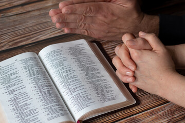 Sticker - hands praying together in faith with an open holy bible book on wooden background. christian husband