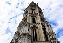 Stone Bell Tower Closeup Of The Matthias Church In Budapest, Hungary. Steep Perspective View. Religious Architecture. Blue Dramatic Sky. White Clouds. Architecture, Travel And Tourism Concept 