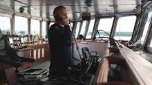 
Male Deck Officer Calling Traffic Control By VHF Radio On Navigational Bridge. Seaman On Board Of Vessel. Commercial Shipping.