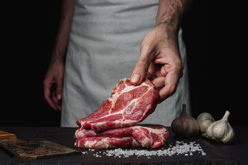 The hand of the cook holds a slice of raw fresh meat on a black background.