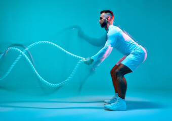 Athletic man training with rope. Side view. Motion blur, long exposure. Fitness sport club advertising. Burning workout