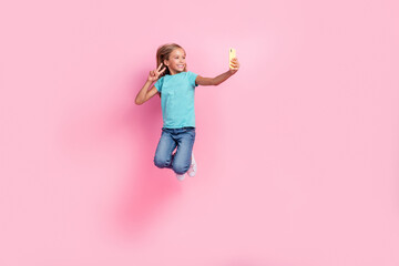 Sticker - Full length photo of adorable cute small kid wear turquoise t-shirt jumping high recording video vlog v-sign isolated pink color background