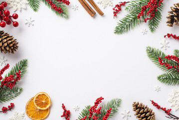 Christmas Eve concept. Top view photo of fir branches in frost mistletoe berries pine cones cinnamon sticks dried orange slices snowflakes on isolated white background with blank space in the middle