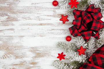 Poster - Christmas side border of red ornaments, snowy branches and  red and black check plaid bow and ribbon. Top down view on a white wood banner background. Copy space.