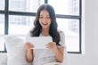 © kaew6566 - Excited asian casual woman reading surprised news with tablet sitting beside window at home. Freelancer young girl search web online looking tablet expression amazed shock open mouth successful news.