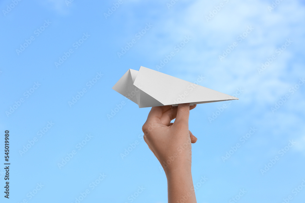 Woman with paper plane against blue sky, closeup