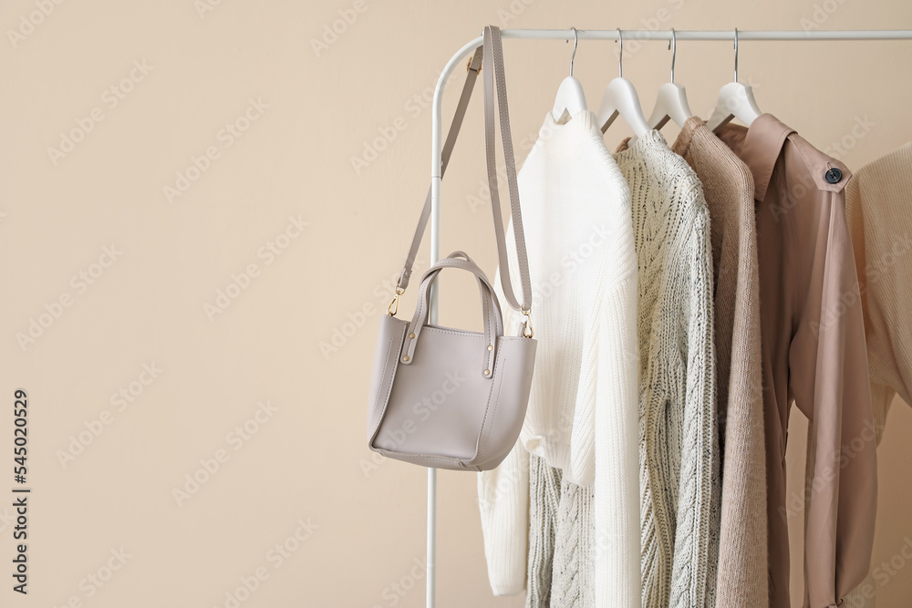 Warm female clothes hanging on rack near color wall