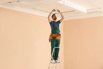 Poster - Electrician in uniform with insulating tape repairing ceiling wiring indoors. Space for text