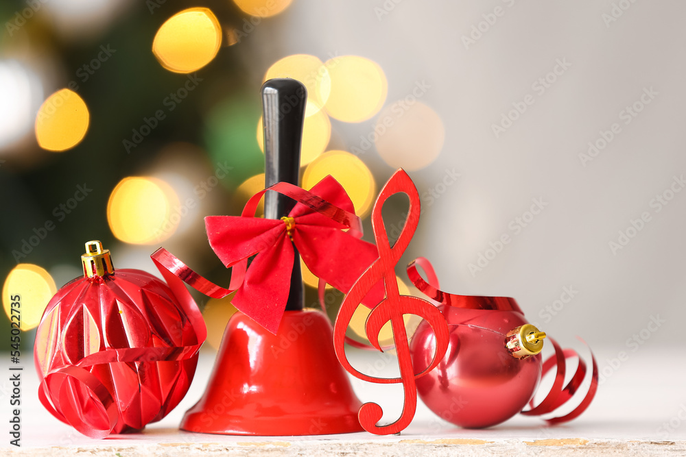 Treble clef with bell and balls on table against blurred Christmas lights