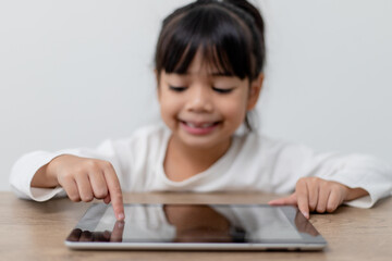 Asian little cute girl touching the digital tablet screen on the table