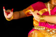 Indian Bharatanatyam classical dancer demonstrating dance mudra or gestures in traditional costume on dark background.