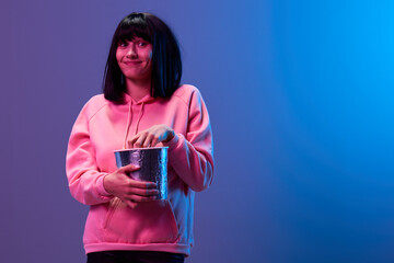 Wall Mural - Funny happy awesome brunet woman in pink hoodie eat popcorn look at camera posing isolated in blue violet color light studio background. Neon party Cyberpunk Cinema concept. Copy space