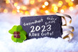 Neujahr Grußkarte 2023, deutscher Text - Gesundheit, Glück, Erfolg, Alles Gute - Schiefertafel mit Kleeblatt im Schnee, Goldene Lichter im Hintergrund - Happy New Year 2023