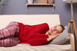 Image of calm tired Caucasian woman wearing red sweater and checkered pants lying on sofa in home interior, keeps closed eyes and sleeping, having nap.