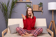 Image of angry astonished Caucasian woman wearing red sweater and checkered pants sitting on sofa in home interior, talking on phone, hearing shocked news, raised arm.