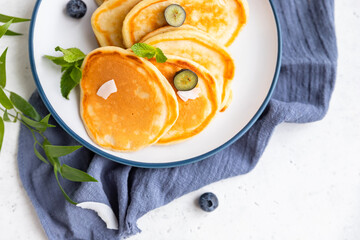 Wall Mural - Traditional fluffy pancakes with orange jam, blueberries, coconut chips and mint for healthy breakfast, light background. High key photography.