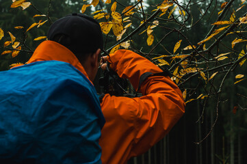 Wall Mural - a man with a camera photographs a dark forest with a large tourist backpack landscape tourism travel recreation hiking trekking creations beauty of nature autumn in the mountains poster postcard