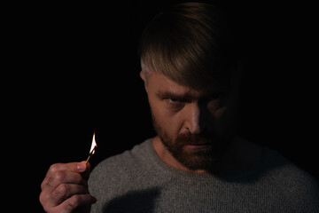 Wall Mural - angry man holding lit match and looking at camera during power blackout isolated on black.