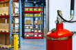 Fire safety equipment. Big red fire extinguisher inside warehouse. Storage room with large fire extinguisher. Warehouse racks with boxes in background. Flame extinguishing equipment.