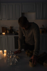 Wall Mural - man standing in dark kitchen near stock of canned food with bottled water and candles.