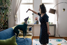 Side View Of Woman Giving Obedience Training To Dog Standing On Sofa At Home