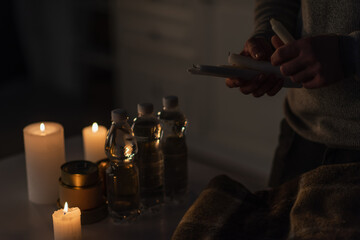 Wall Mural - partial view of man holding candles near bottled water with canned food and warm blanket on table.