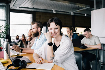 Portrait of smiling non-binary business person sitting by male programmer at desk in office