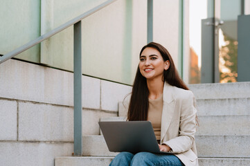 Young indian student woman working with laptop while sitting on stairs