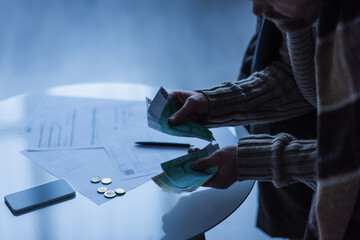 Wall Mural - partial view of man counting money near smartphone and payment bills in twilight.