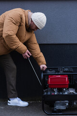 Wall Mural - side view of man in down jacket and knitted hat starting electricity generator outdoors.