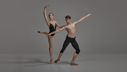 Wall Mural - Young man and woman, ballet dancers performing isolated over dark grey studio background. Artistic movements