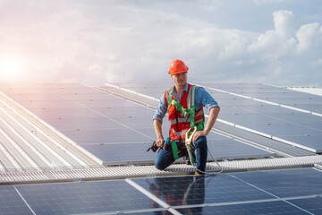 Poster - Technician wearing safety harness belt using drill during installing the solar panels on roof structure of building factory.
