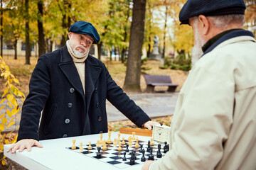 Wall Mural - Portrait of two senior men playing chess in the park on a daytime in fall. Difficult game. Concept of leisure activity, old generation