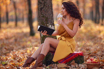 the beautiful woman is reading a book with a glass of wine in her hand during autumn