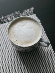 Sticker - Vertical top view of a cup of foamy latte on a checkered towel on top of a black table