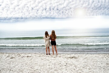 Closeup of two teen girls standing on a sandy beach enjoying the view of the sea