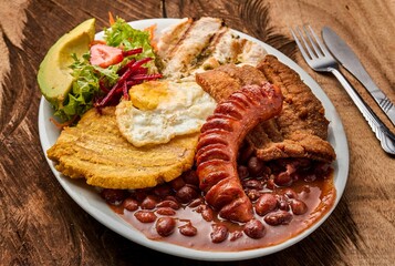 Sticker - Top view of a white plate with Bandeja paisa with an egg, and vegetable salad on a wooden table