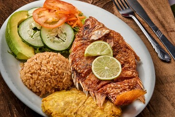 Poster - Top view of a white plate with Pescado Frito, rice, and a vegetable salad on a wooden table