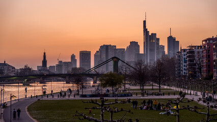  Beautiful shot of a crowded park against modern buildings in Frankfurt, Germany at sunset