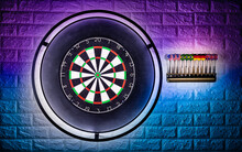 Professional Sisal Steeldart Board With Steel Dart Holder In Colorful LED Illumination White Stone Wall. Leisure Time Hobby Sport Concept Background.