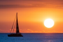 Silhouette Of A Sailboat In The Ocean Against The Golden Sunset Sky Under A Golden Sky
