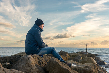 Man sitting alone on rocks looking at the sea.