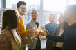 © maxbelchenko - Toasting to success concept.Group of young business people toasting each other and smiling while standing in the office. Celebration and festive concept.